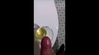 A guy in sweatpants pisses and cums in a glass for his friend, who then drinks it