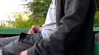 A guy in public pisses and jerks off his cock on the river bank, and a fisherman is fishing nearby