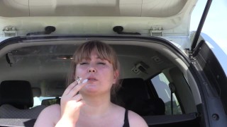 A cute bbw smokes in the street near the car