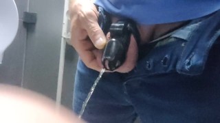 Locked in a chastity cage, man is pissing in a public toilet