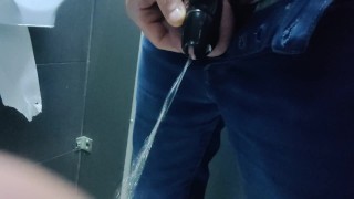 Locked in a chastity cage, man is pissing in a public toilet