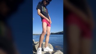 Twink boy with long dark hair pissing pee on the river dressed in glasses cap sneakers boxer tshirt