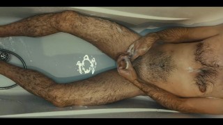 Hairy guy soaps up in bath, strokes, plays with his dick and foreskin and pisses on himself
