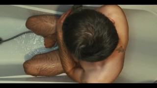 Hairy guy soaps up in bath, strokes, plays with his dick and foreskin and pisses on himself